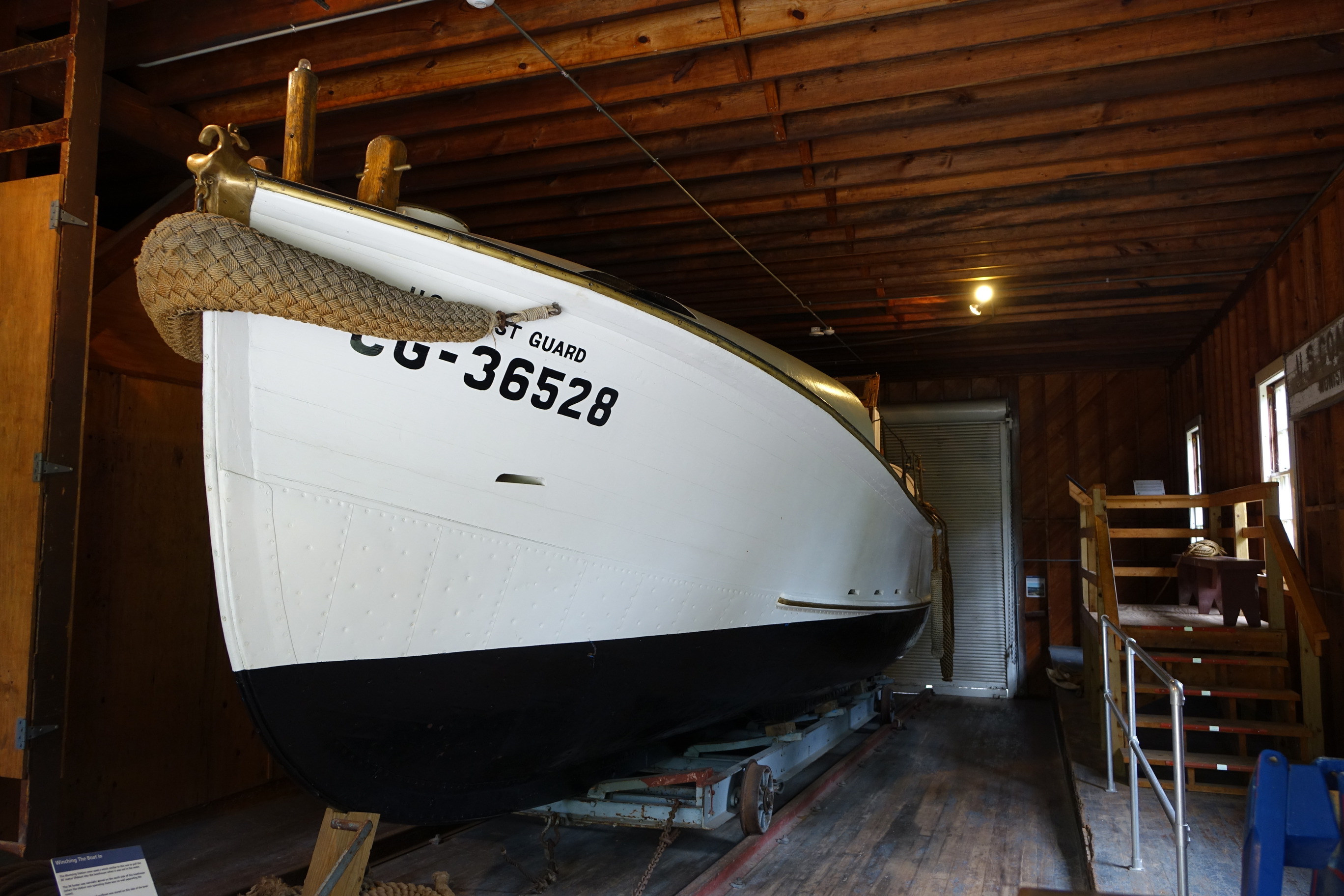 The thirty-six foot boat is in a wooden building. The boat sits on a low wheeled cradle that is on rails. 