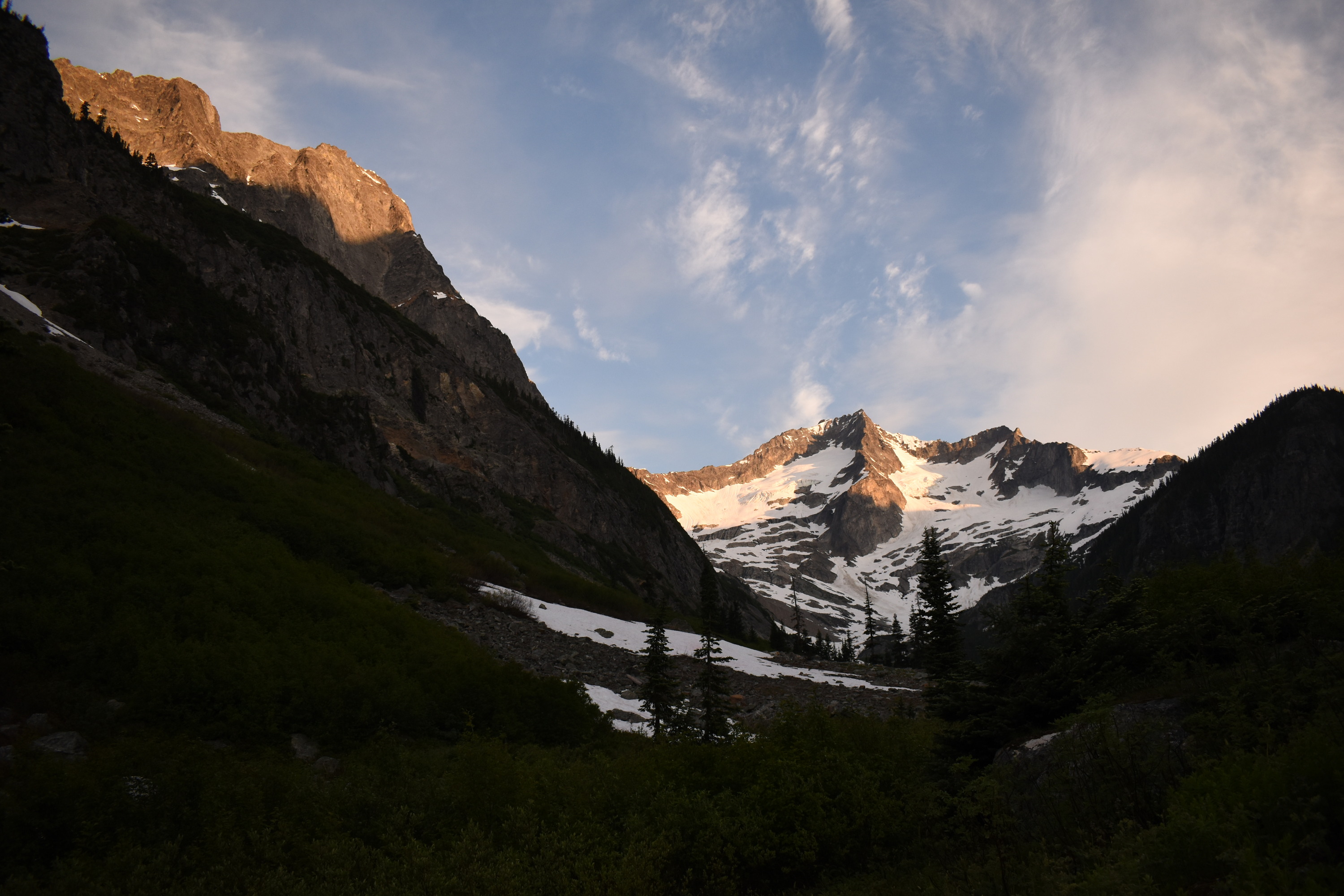 A snow-capped peak with a steep cliff on the left glow peach in sunrise.