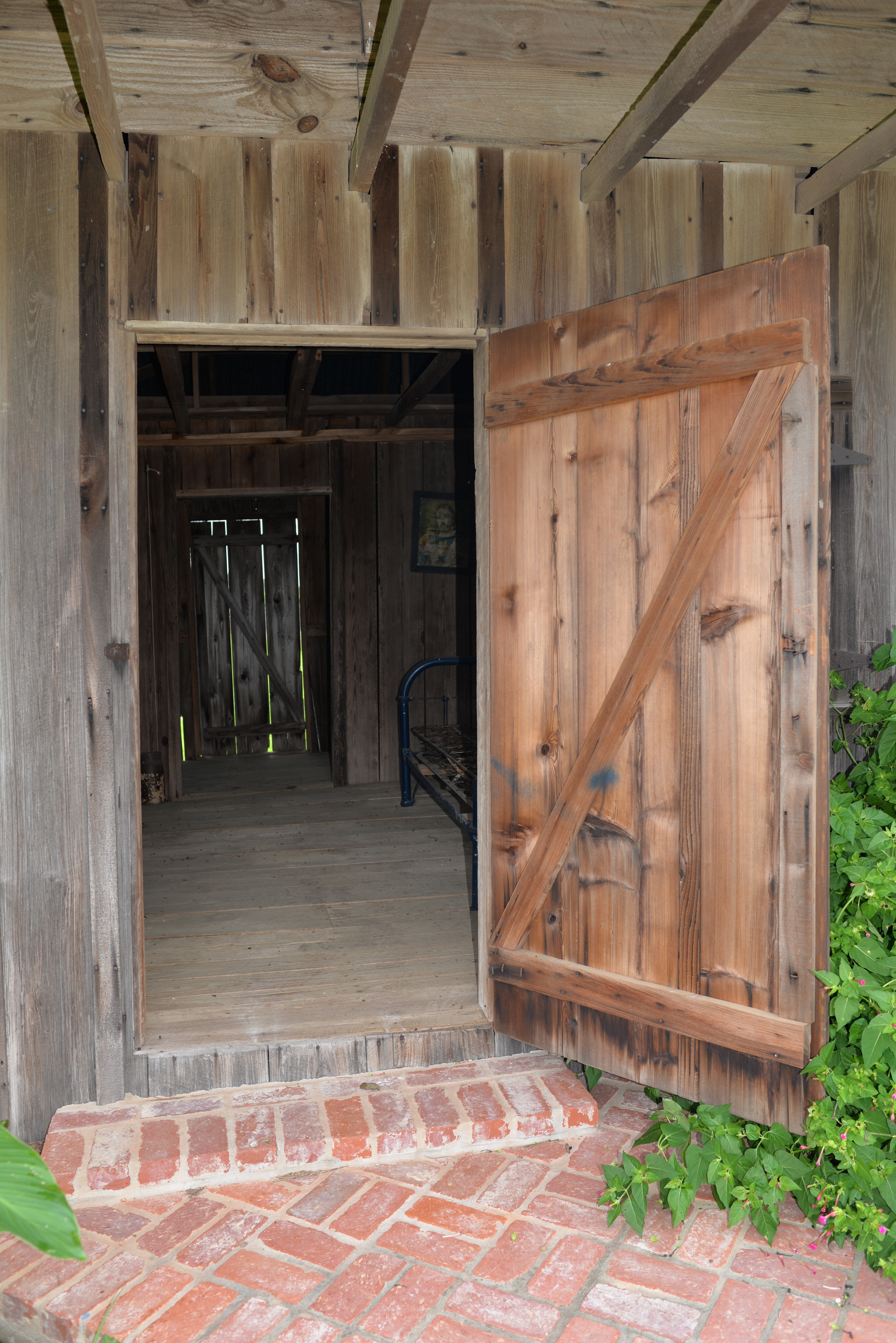 Wooden door to cabin is open, exposing the wooden interior. A brick walkway leads to the door.