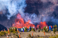 Visitors stand at a craters edge looking at an eruption within a crater. 