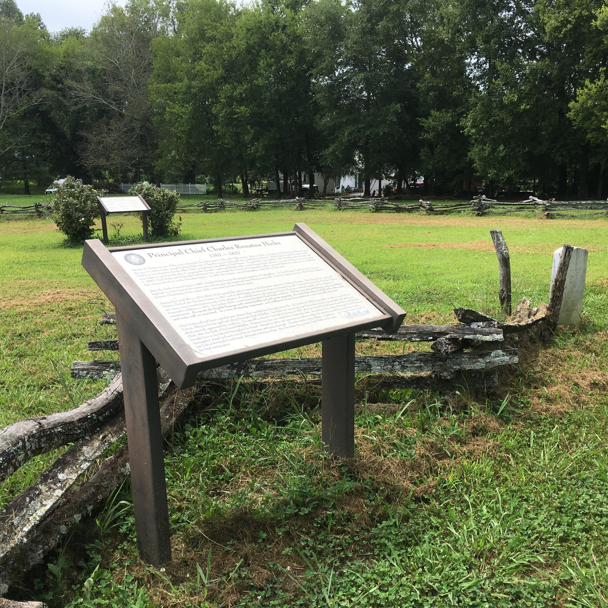 A wayside in front of a wooden fence in the middle of a grassy field.