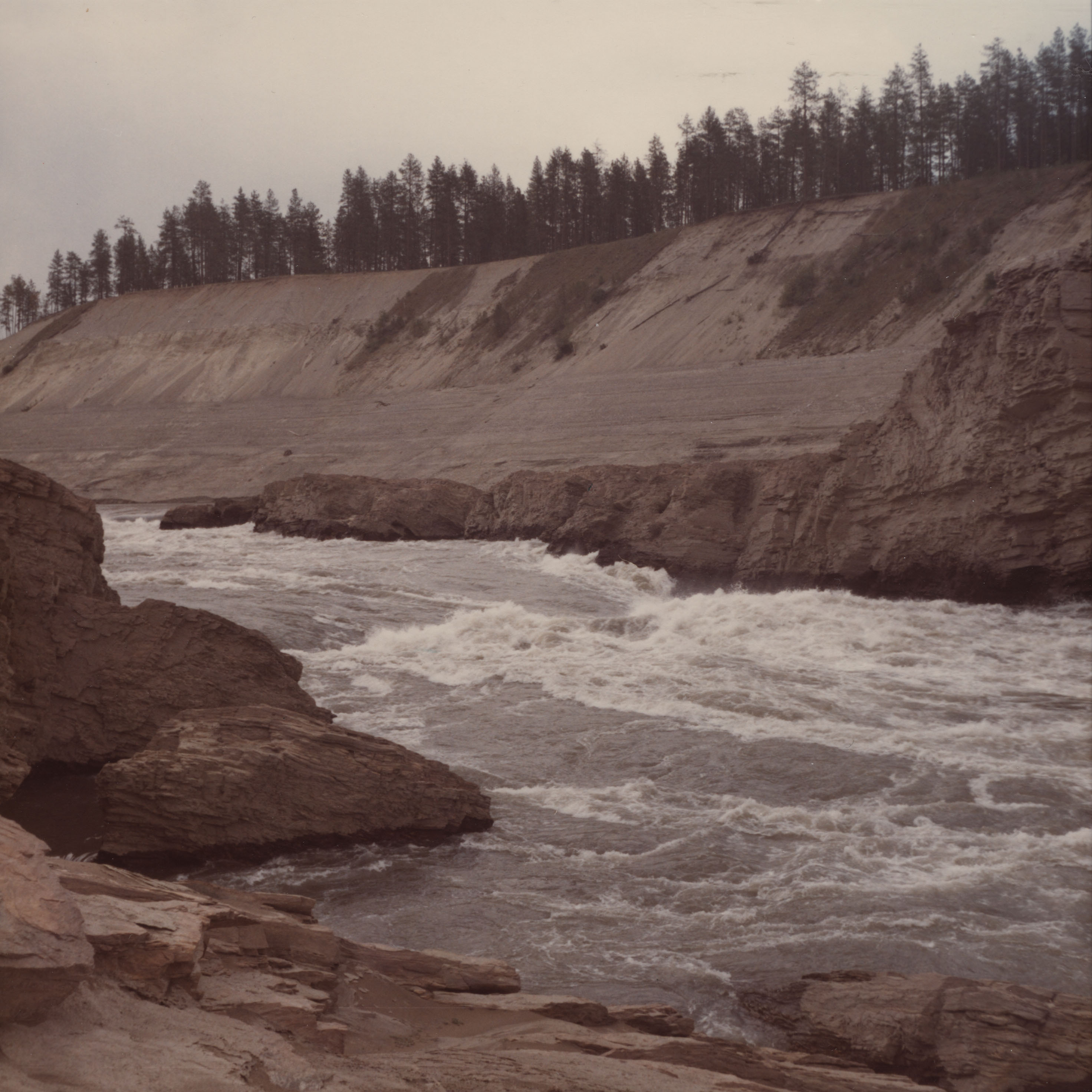 Color photograph of river rushing past steep cliff of loose rock