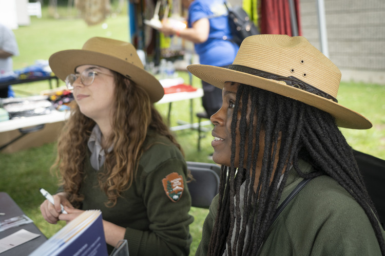 Two female park rangers in uniform, sitting at a table outdoors. 