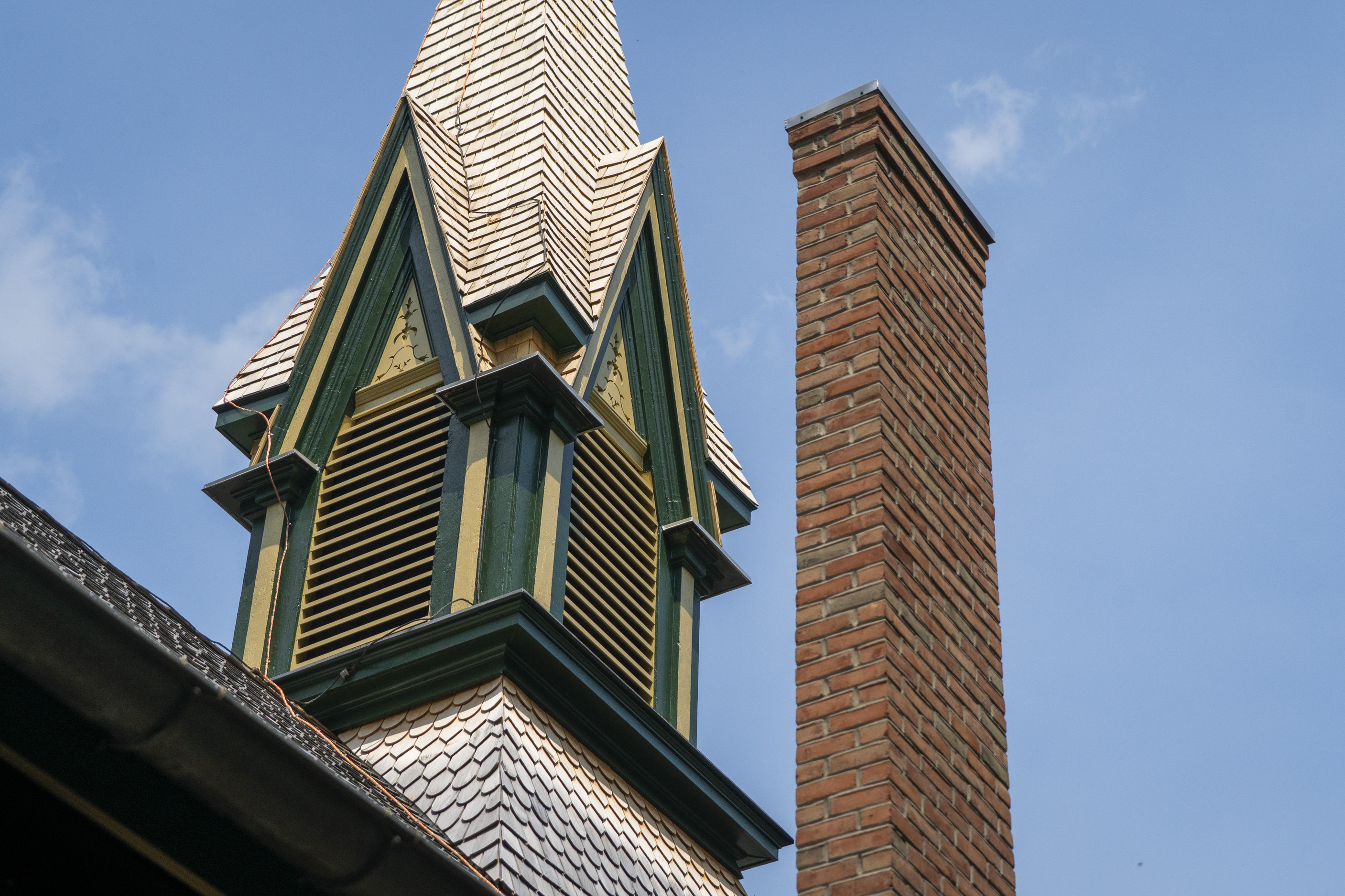 A green and yellow church steeple alongside a brick chimney.