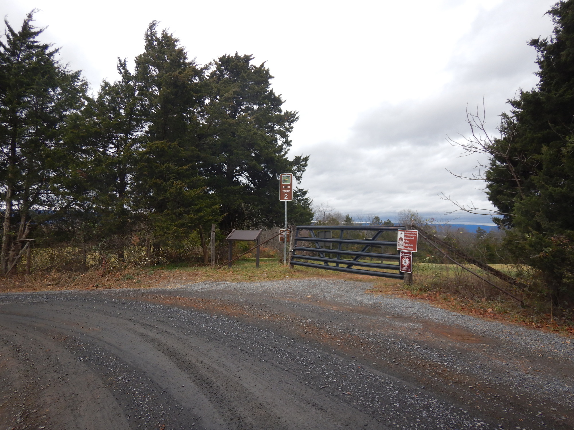 Brown street signs posted by a swing gate mark a stop along a historic battlefield. 