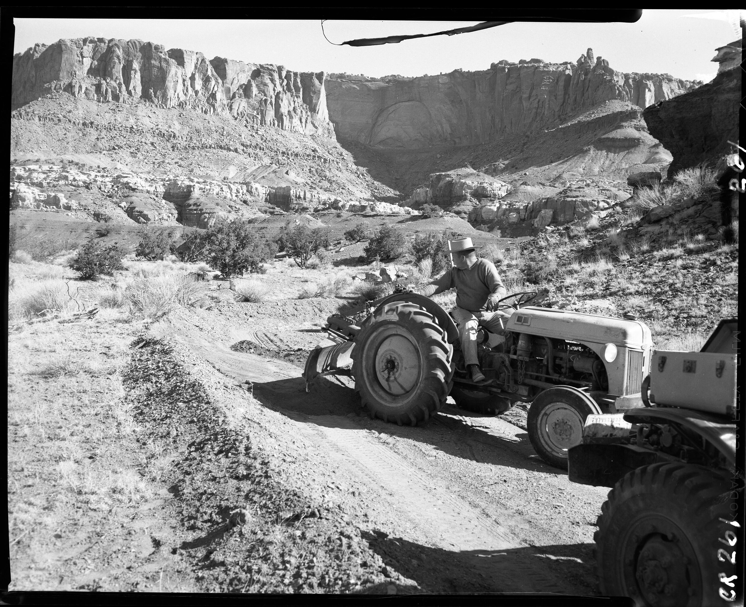 Man on tractor pulling a grater, with cliffs in the background. 