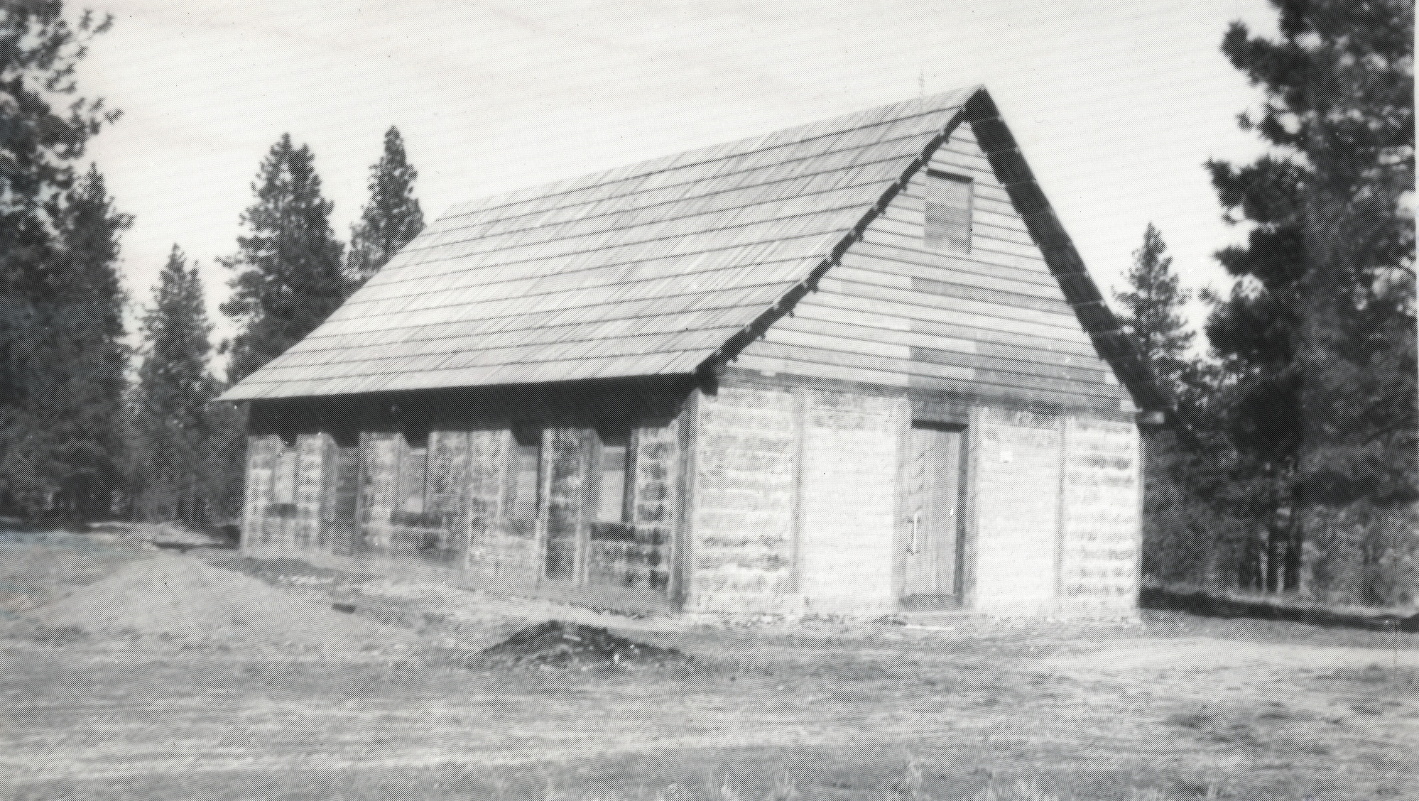 Black and white photograph of a plain wooden buildings in a forest