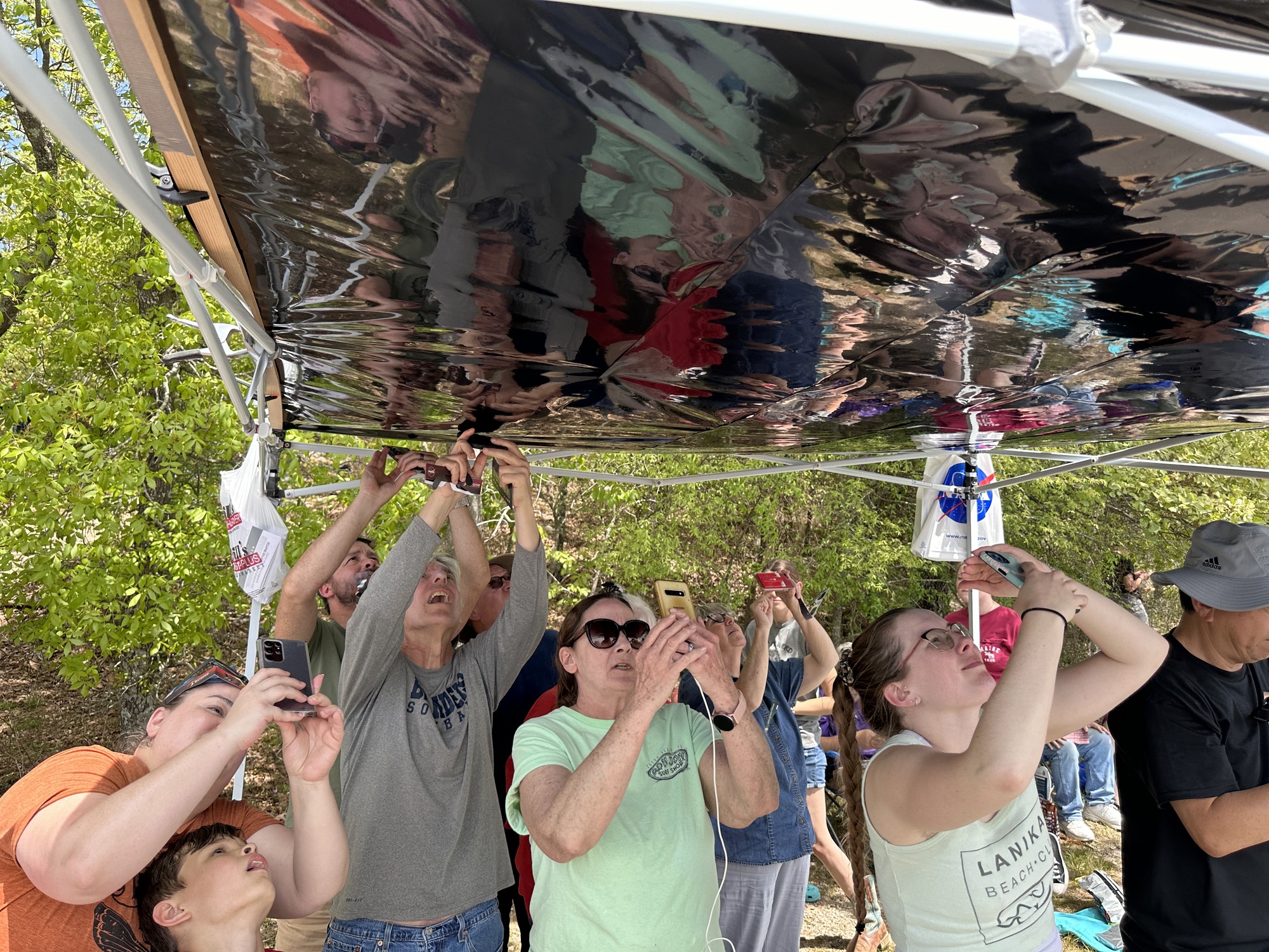 A group of people point cameras through an overhead tarp made of dark material.