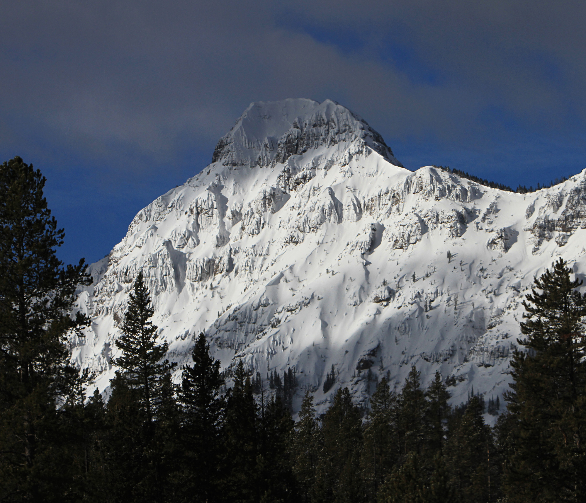 The top of a snow covered mountain has a blue sky background.