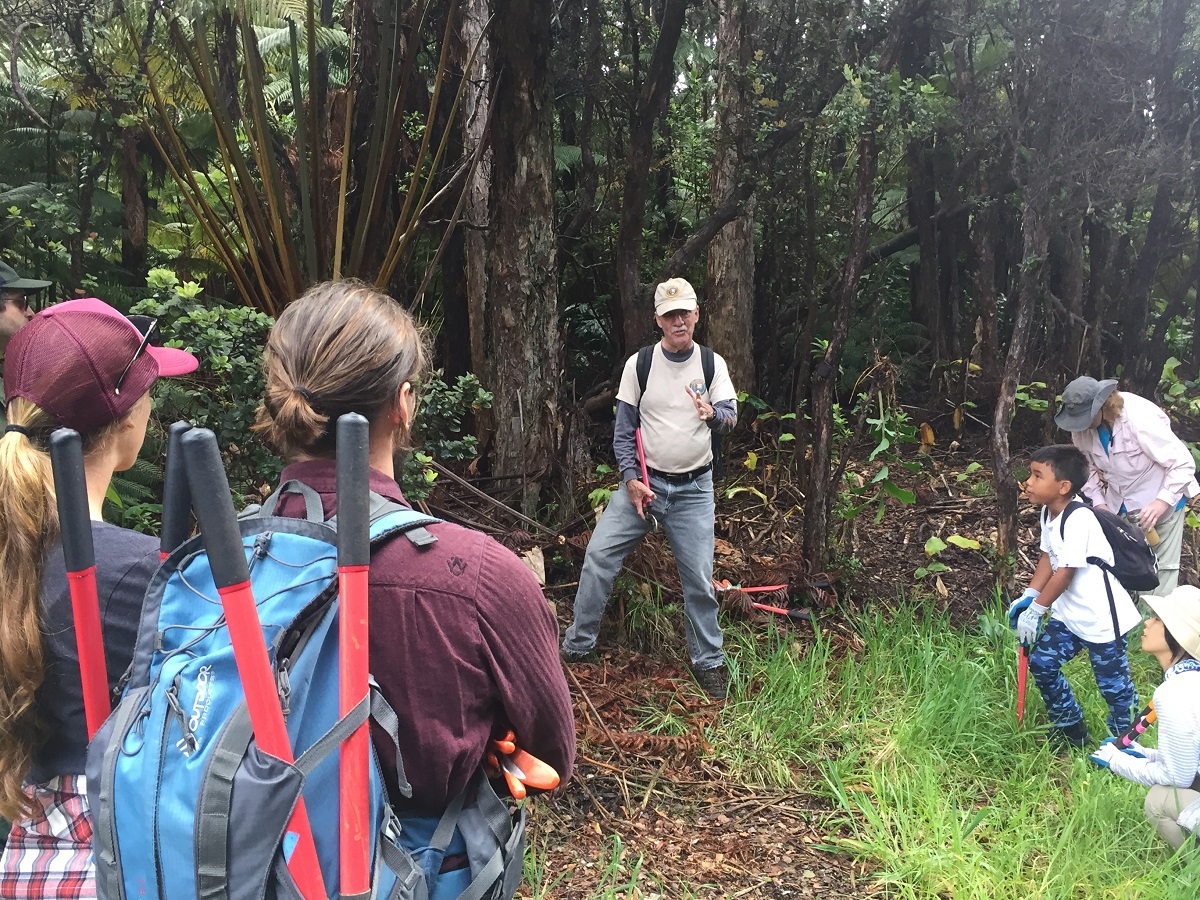 A man wearing a ball cap addresses a group of volunteers with garden shears before heading into the forest 
