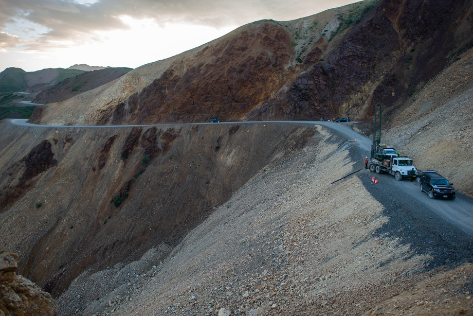 four trucks parked on a dirt road precariously perched on the side of a mountain