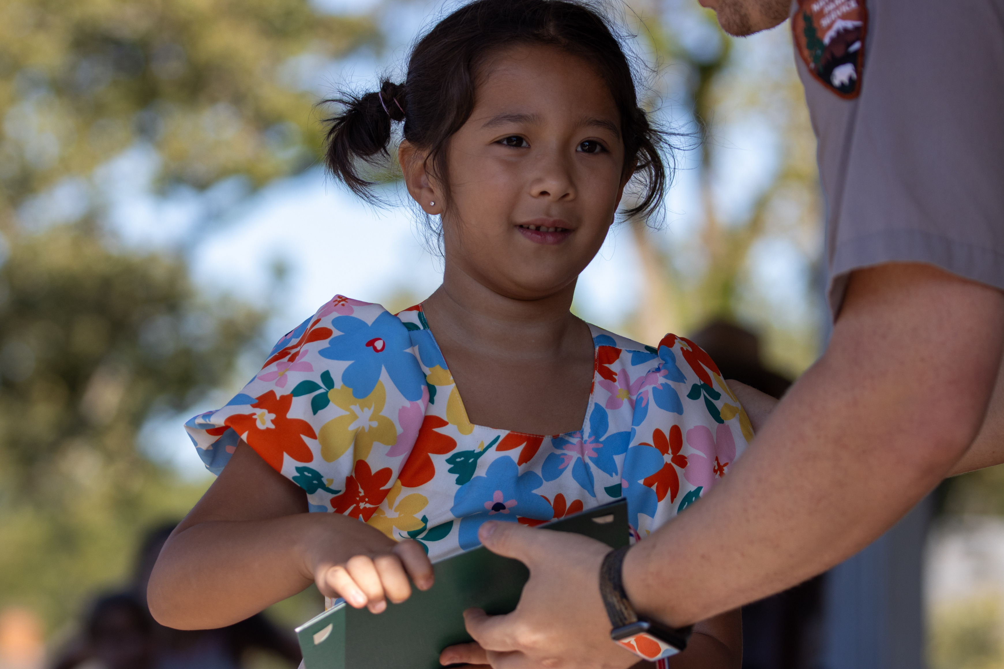Girl in blue, yellow, and red floral dress receiving award during Plains Peanut Postcard Contest awards ceremony.