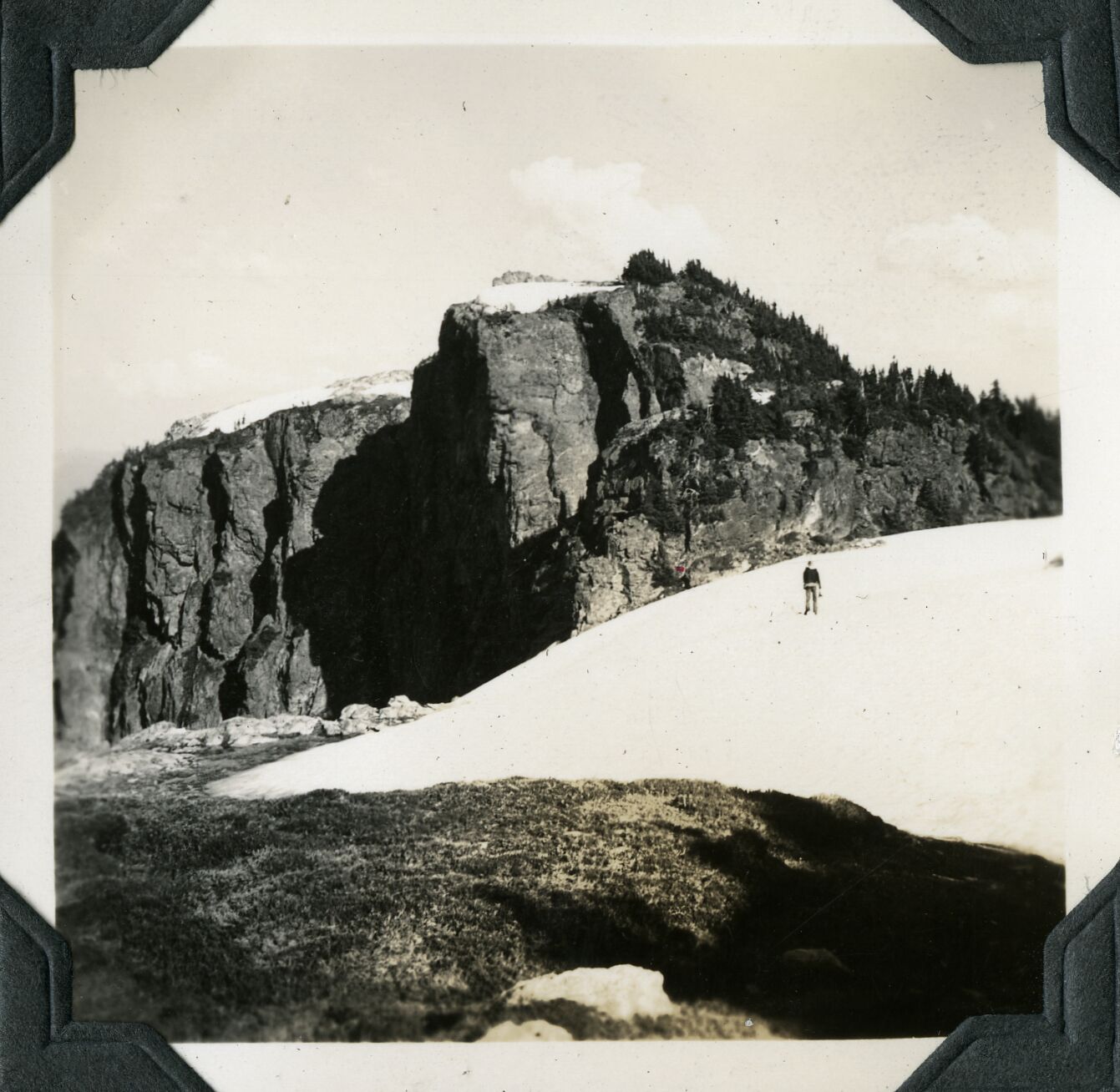 A man standing on a snowfield with rocky prominences in the background.