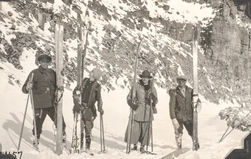 Black and white photo of two men, two women dressed in wool clothing and holding long wooden skies in the snow.