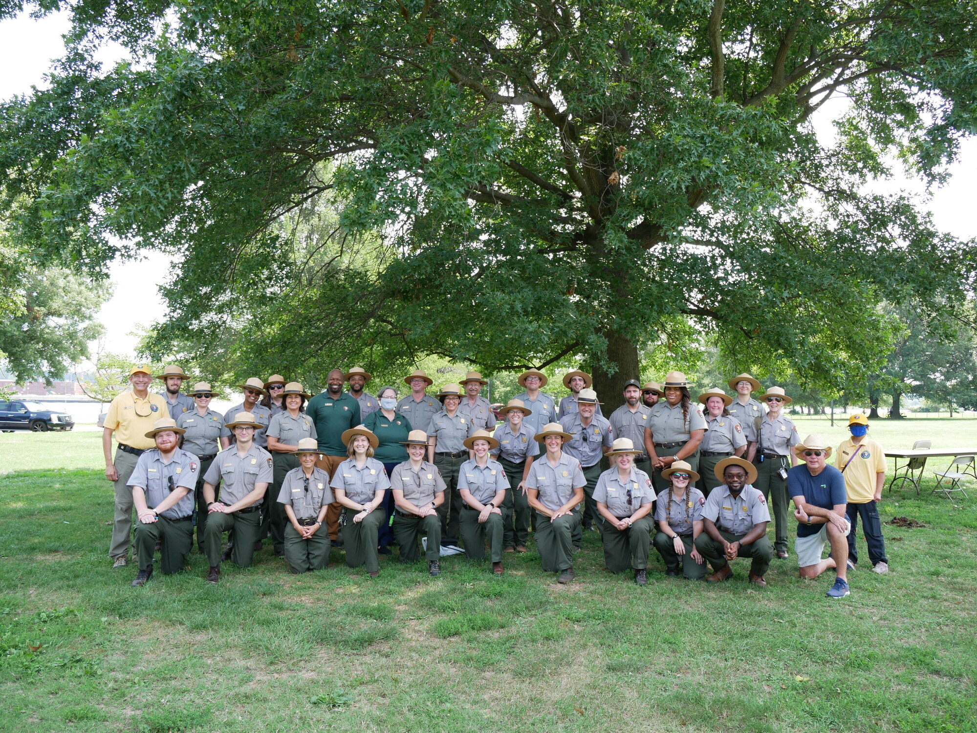 National Mall Park Rangers and staff are kneeling and standing under a large tree after engaging the community during Hains Point Community Day.