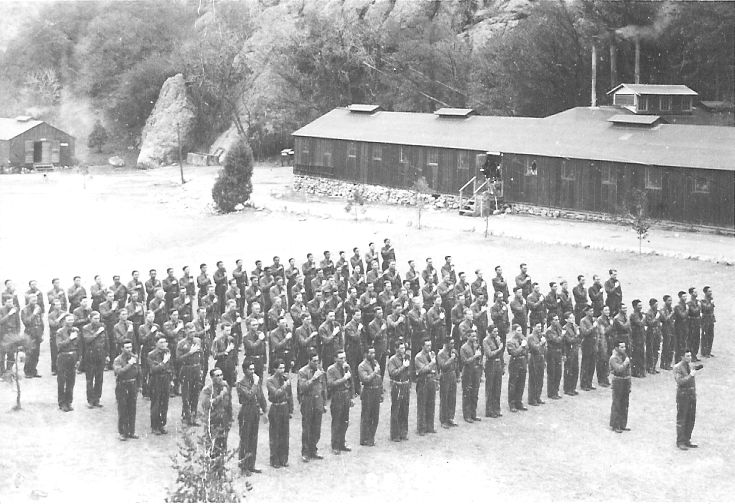 Black and white photo of 4 rows of men with their hands over their hearts. Possibly saying the Pledge of Allegiance to the flag. 