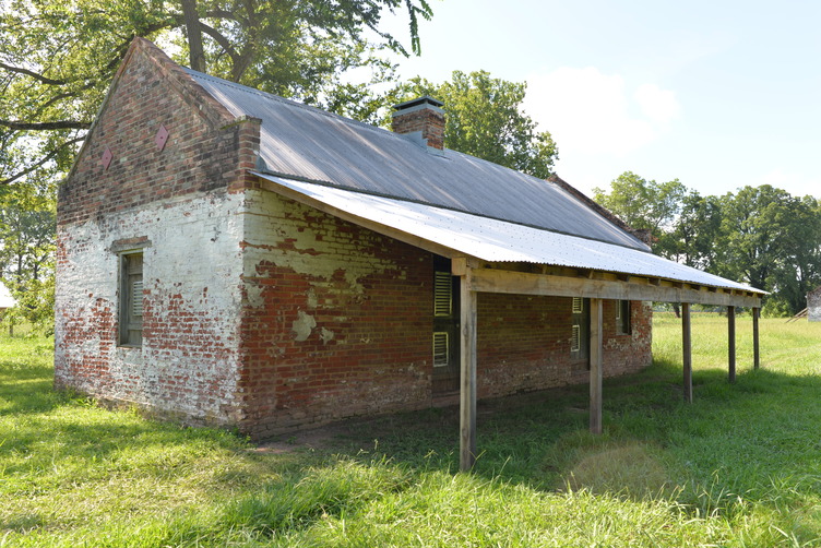 Angled front view of brick structure, a chimney centrally located, and metal roof with awning.