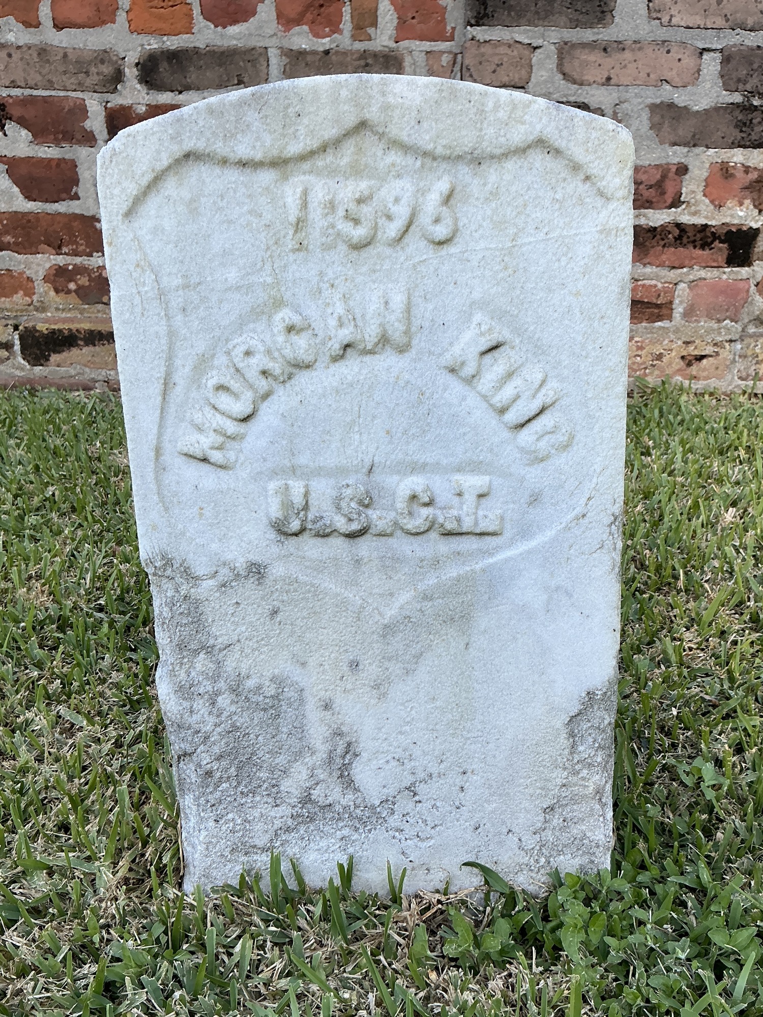 Front of historic upright marble headstone with recessed shield with recessed lettering face.