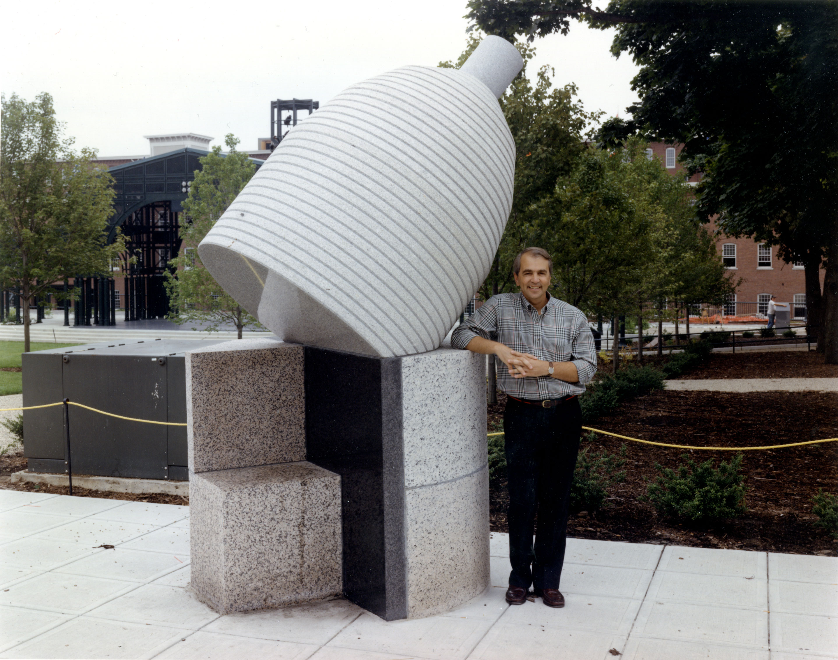A man standing next to an enormous, tipping granite bobbin. 
