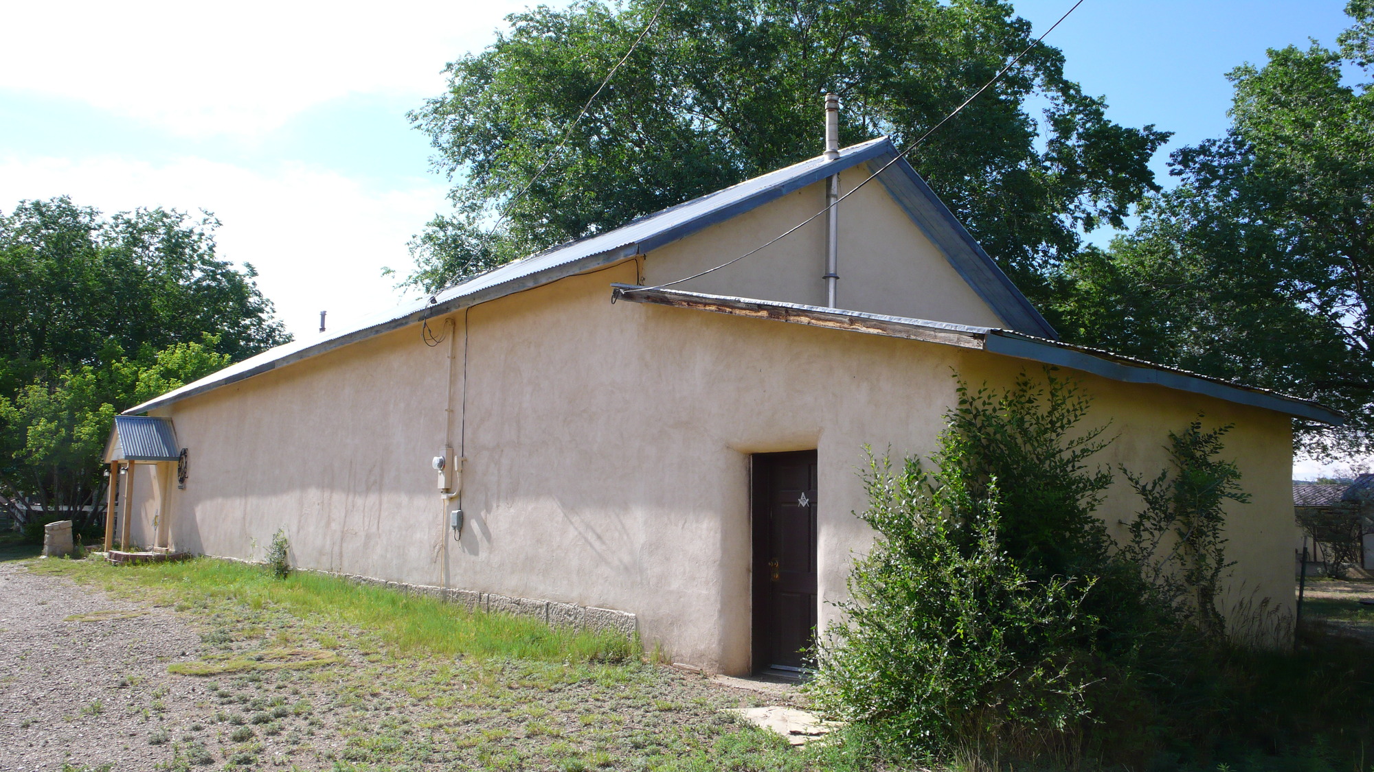 A small tan building with a blue roof with trees in the background.