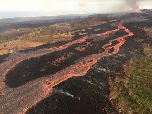 Aerial view of river of lava in a forest with a volcanic cone at the head