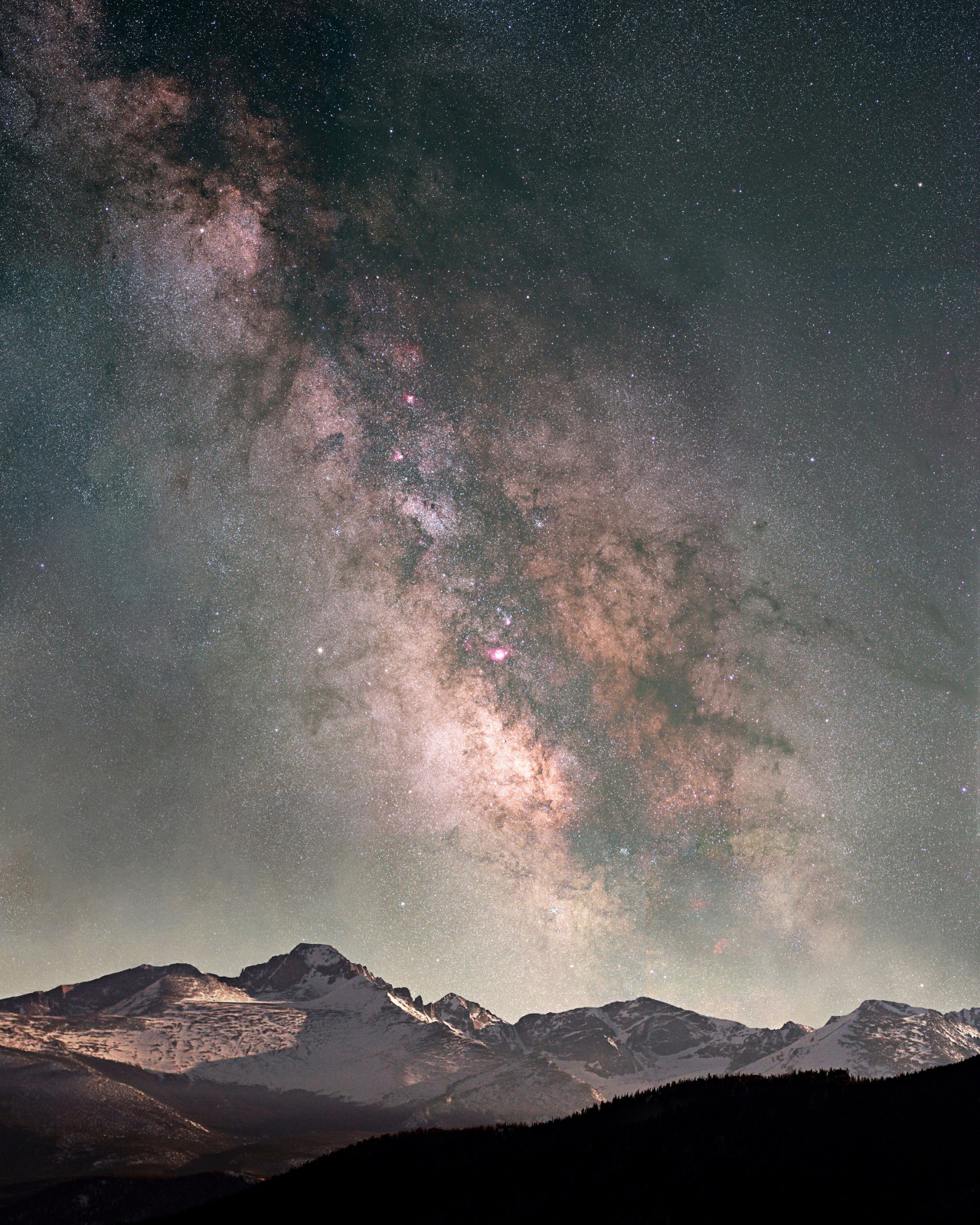 Night sky view of the Milky Way rising above the snow-capped peaks of Rocky Mountain National Park, Colorado.
