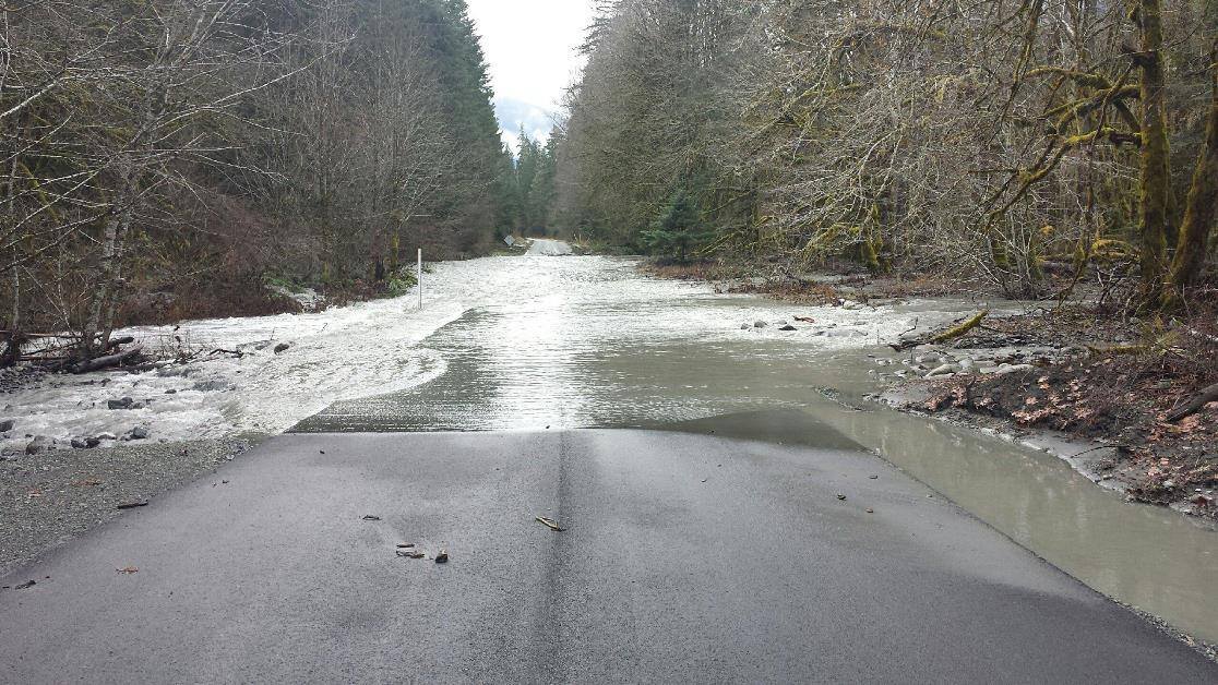 Water flows across a section of roadway with standing water on one side