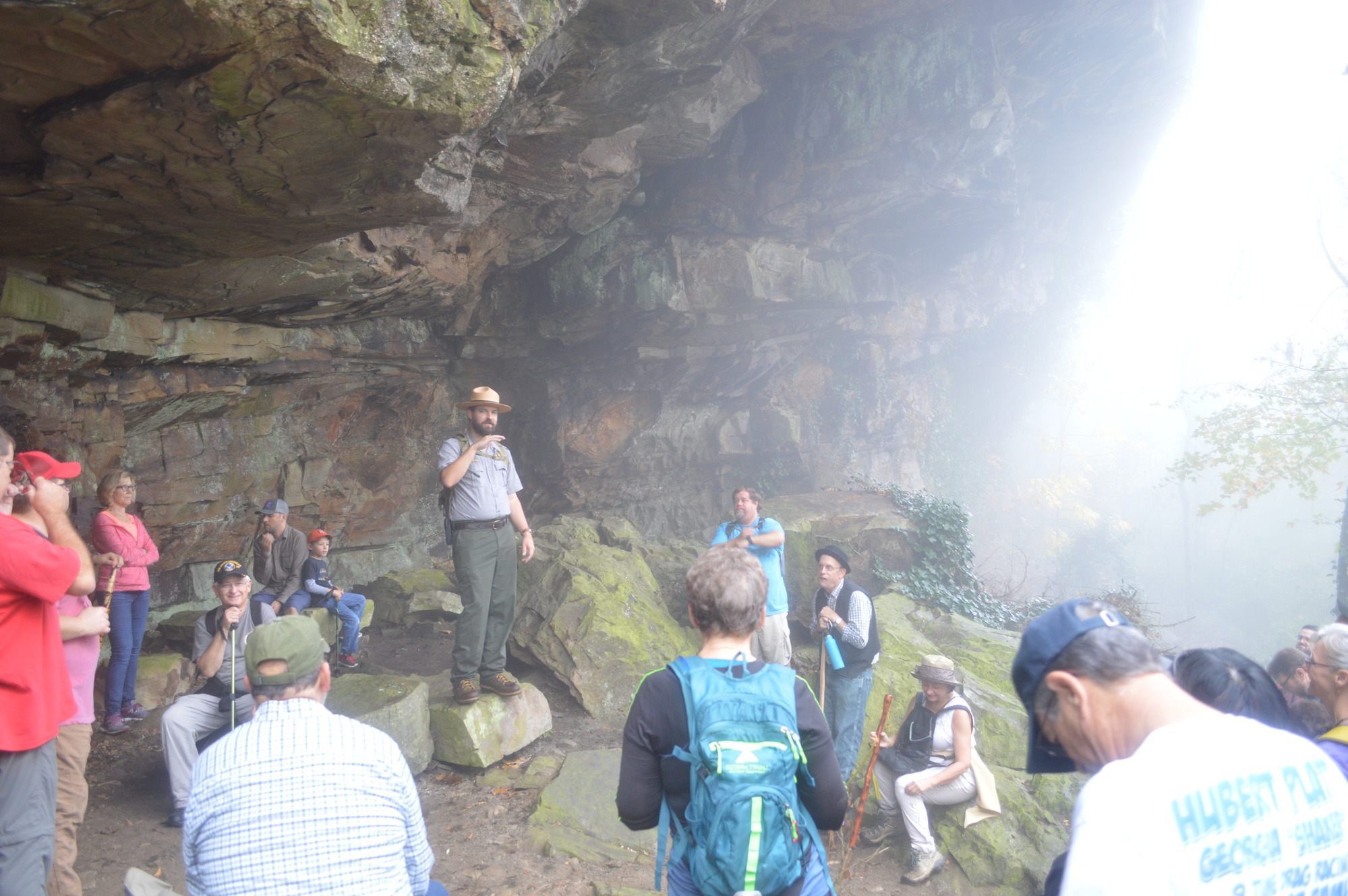 A park ranger talks to a crowd of people along a trail underneath a rocky bluff