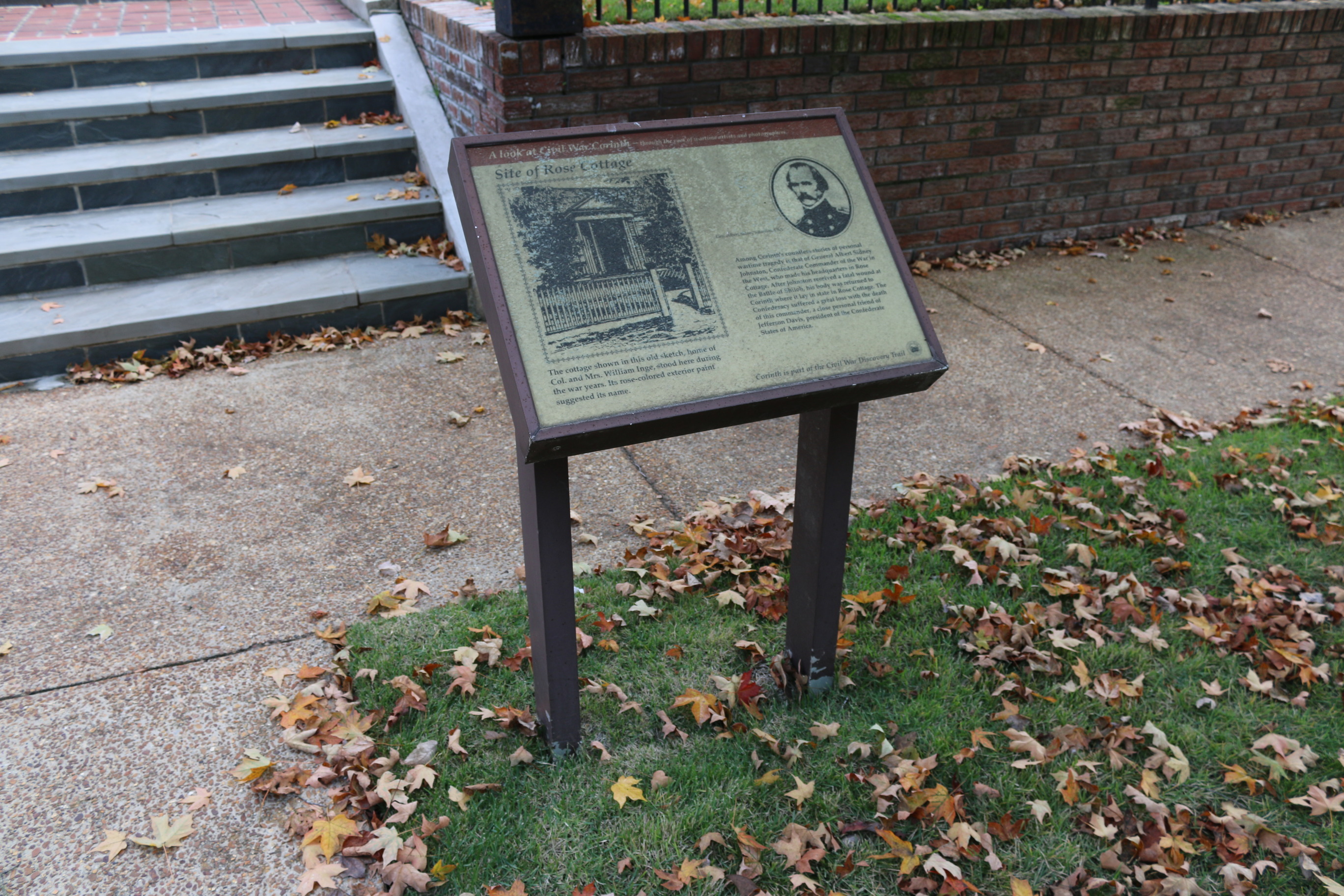 A battered wayside stands near a sidewalk and brick wall.