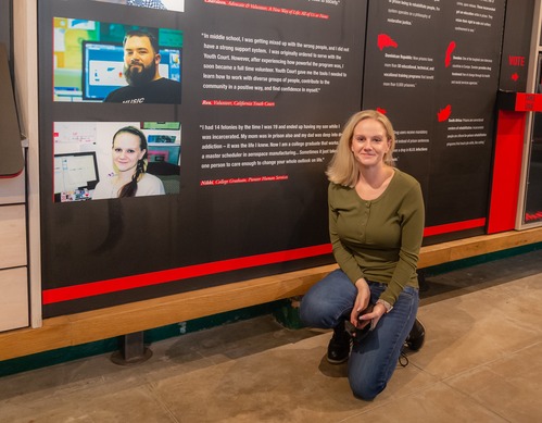 Woman squats next to photo of herself and a block quote of her words on a wall in The Big Lockup.