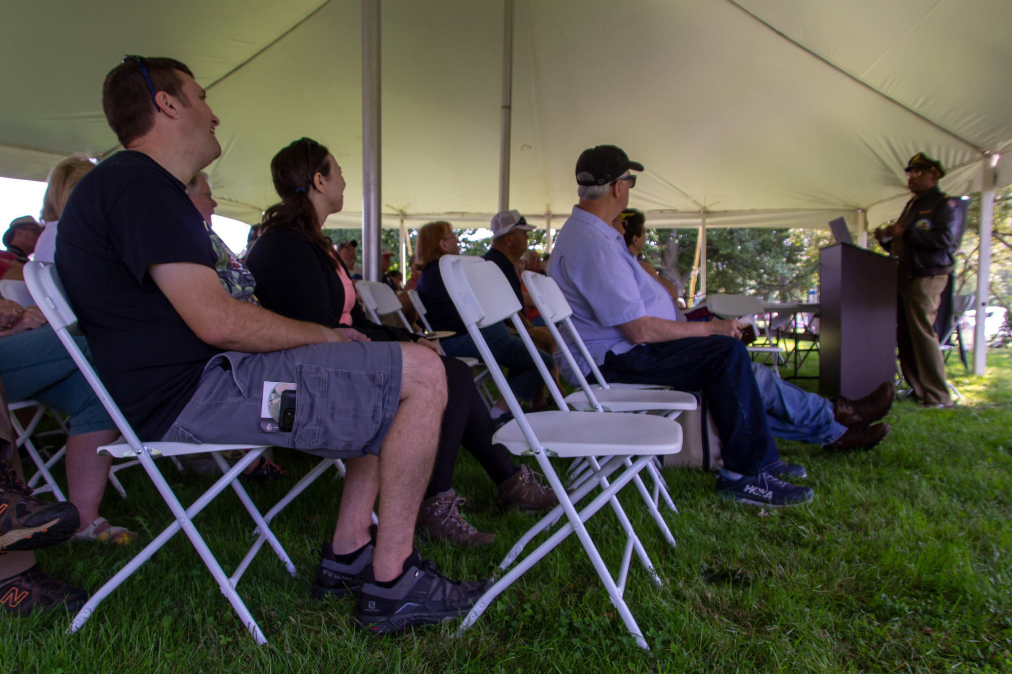 A man in a WWII period military outfit speaking under a tent in front of  a group of people.