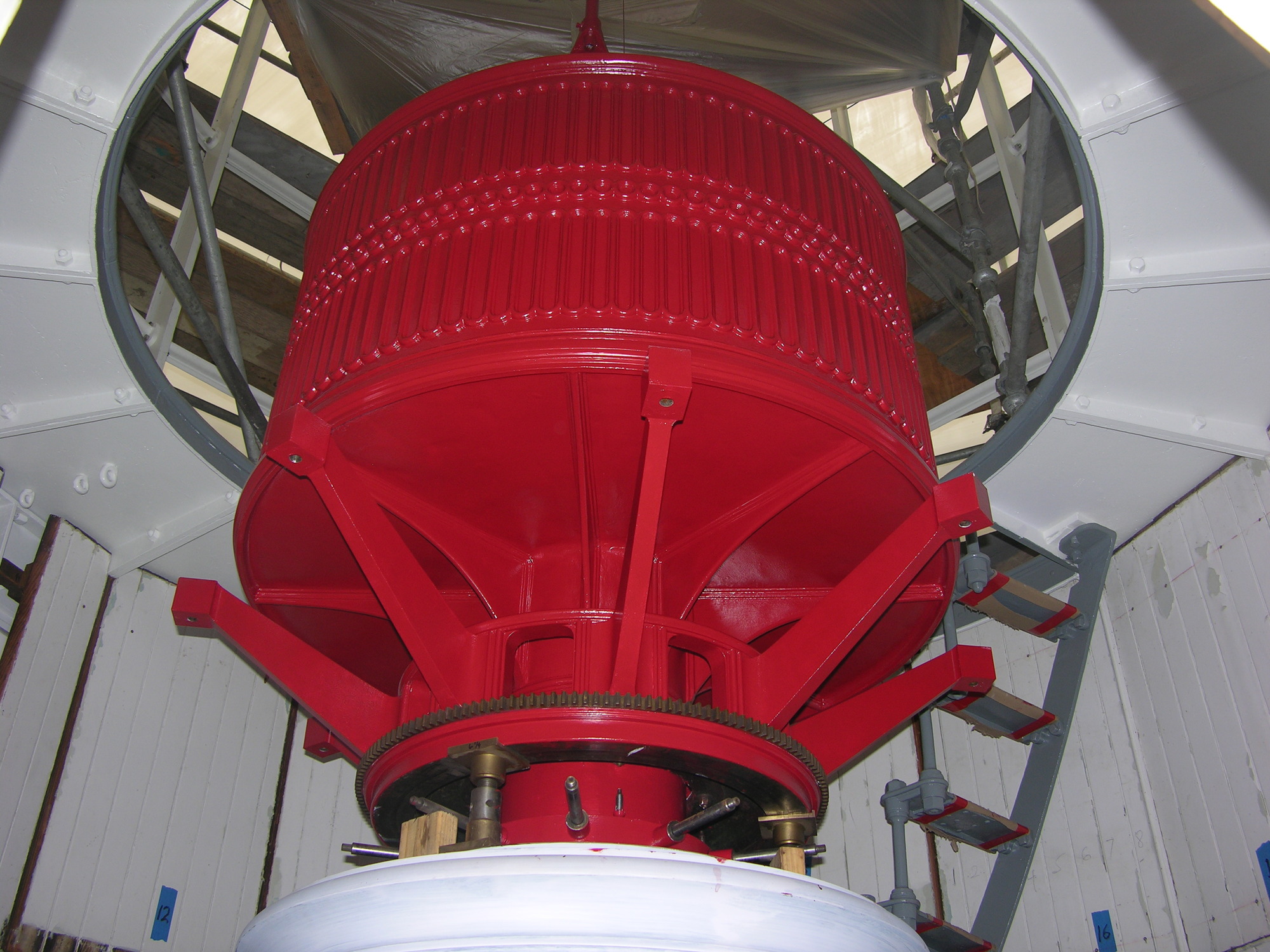 A red cylindrical pedestal rises toward a circular hole in the ceiling of a small room. Eight red arms (five of which are visible) radiate out at forty-five degree intervals around the tapered base of the pedestal.