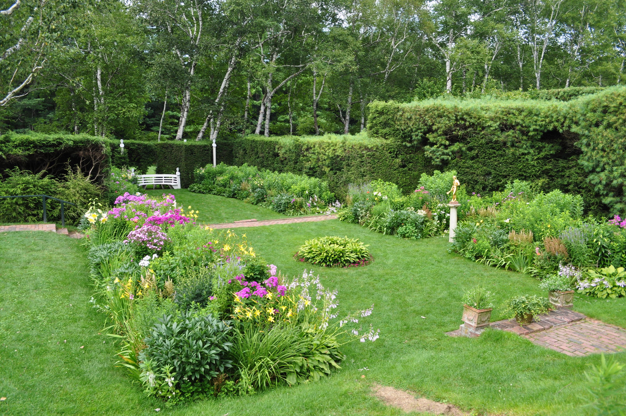 Short grass separates rectangular planting beds with blooming perennial flowers, encircled by a tall hedge. 