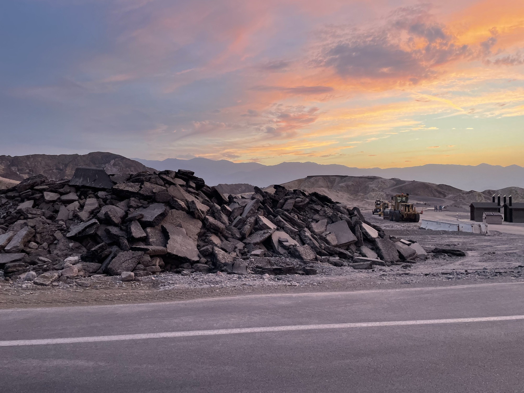 a large pile of pieces of asphalt next to a road with heavy equipment behind in a desert canyon