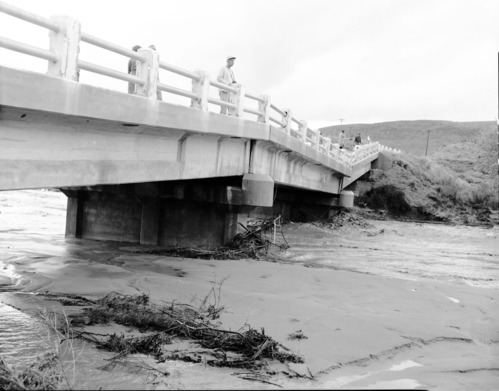 The partial collapse of Coal pits Wash bridge on State Route 15 (now State Route 9) with several people standing on bridge. Note the debris and sandbar in foreground water still flows on both sides of sandbar. [See ZION 8601, 8599, and 8598 also.]