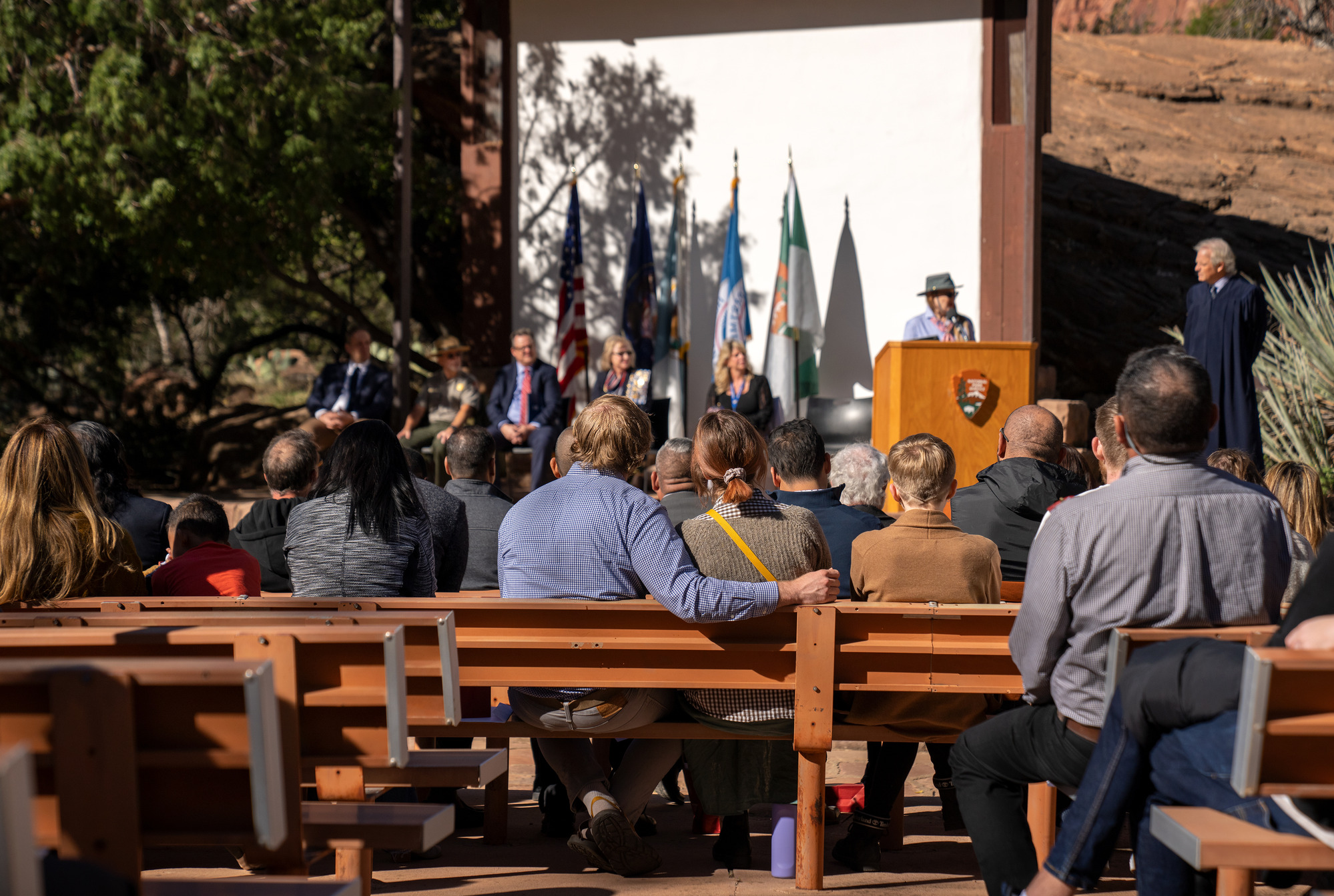The backs of the members of a crowd sitting in front of a stage. 