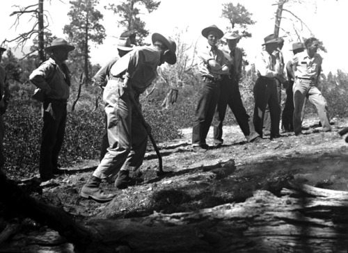 National Park Service Region 3 fire training school. Several rangers looking on at one shoveling near embers of fire.