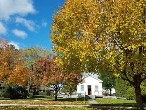 Trees in brilliant autumn foliage frame an old white schoolhouse.