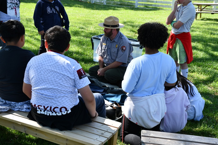 A seated ranger displays replica Civil War soldier uniforms and equipment to fourth graders. 