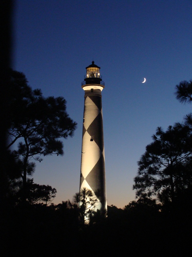 Cape Lookout Lighthouse illuminated with quarter moon in the night sky.