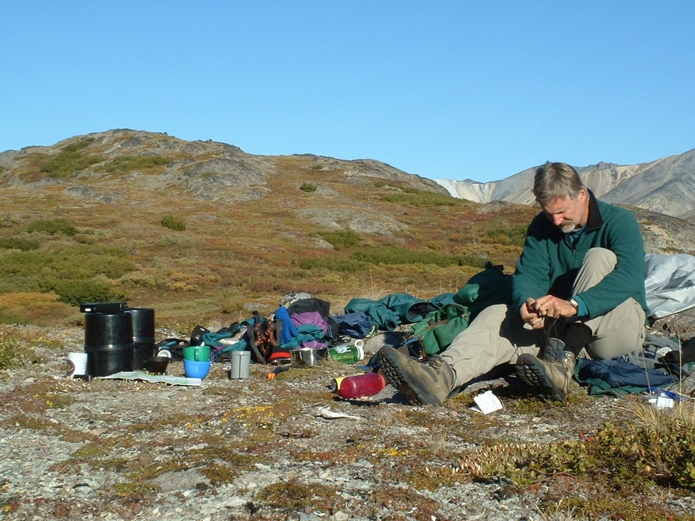 man sitting on the ground, camping gear spread all around him, in a tree-less landscape