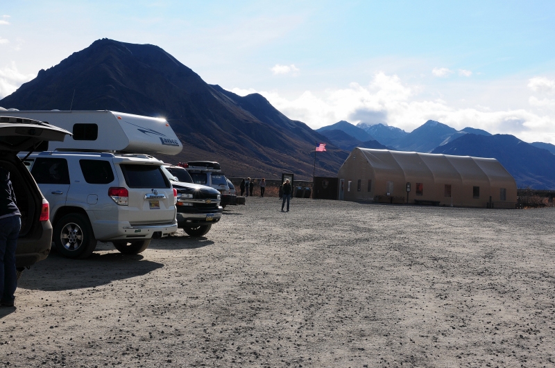 cars parked in a gravel lot, a tall mountain in the distance