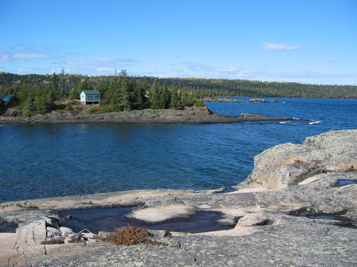 Cabin across a bay perched on the Lake Superior Shoreline. Splash pools on the rocky shoreline in the foreground.