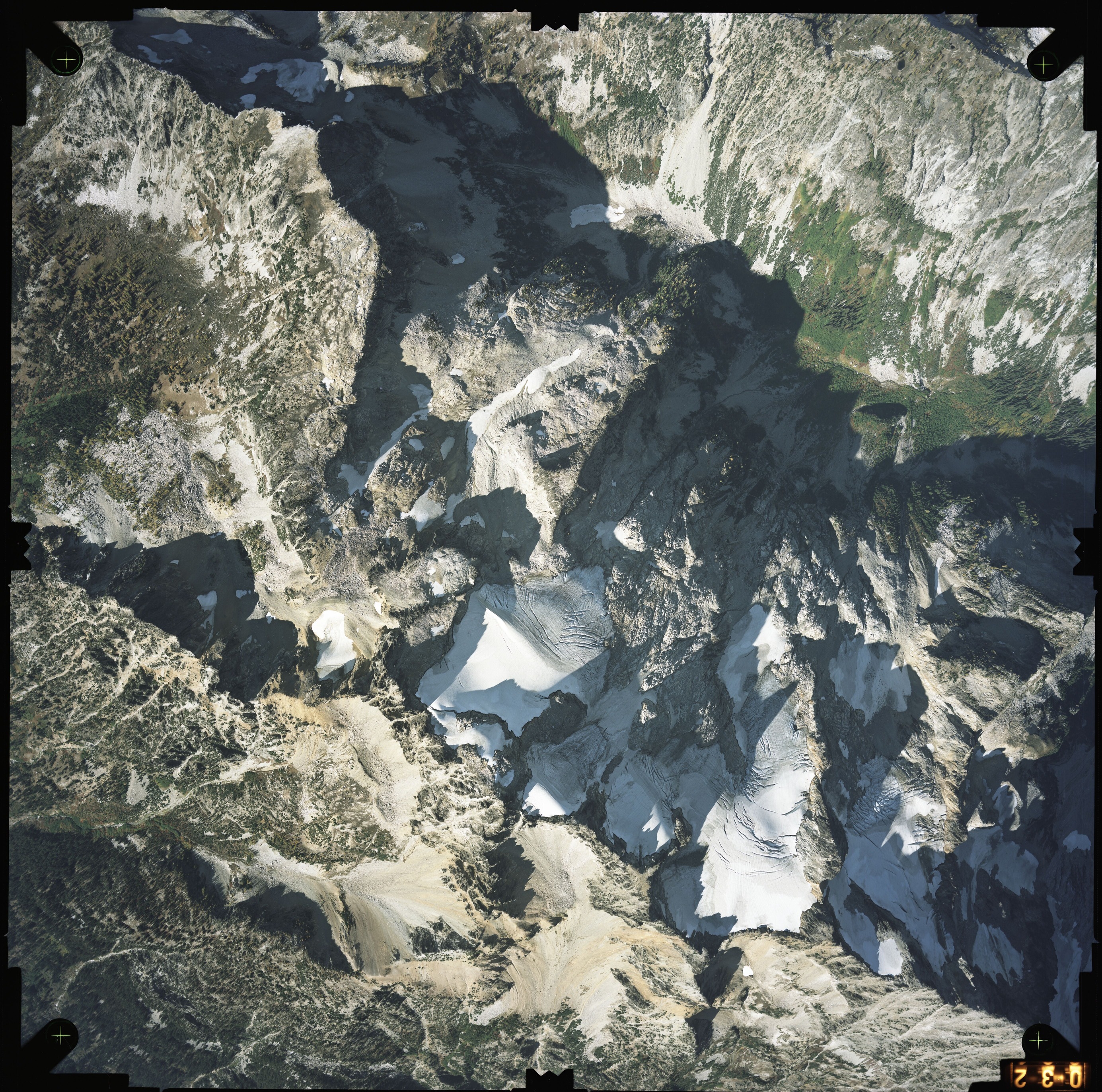 Color aerial photograph of glacier and snowfields on mountain peak with forested valleys below.