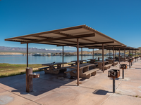 row of picnic benches under shade structure leading away from view, marina in distance