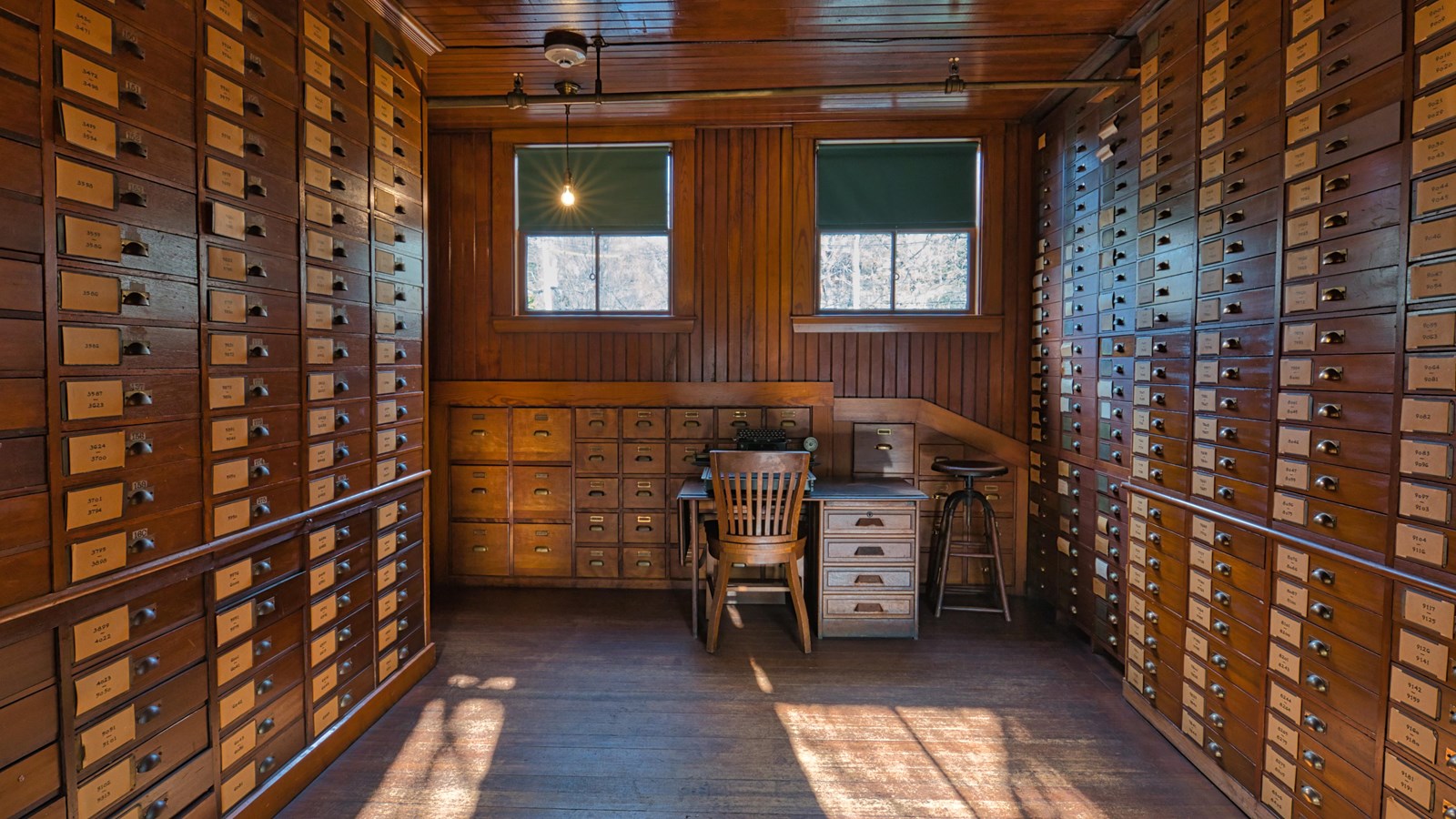 Many wooden boxes line both sides of wall in wooden room, with a desk and chair on the far end 