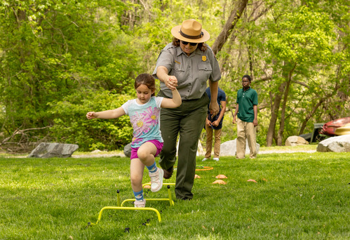 Chesapeake and Ohio Canal National Historical Park Chief of Interpretation, Education, and Volunteers Christiana Hanson helps a little girl traverse an obstacle course meant to simulate the Shad Run at Fletcher’s Cove on Earth Day, April 22, 2025.