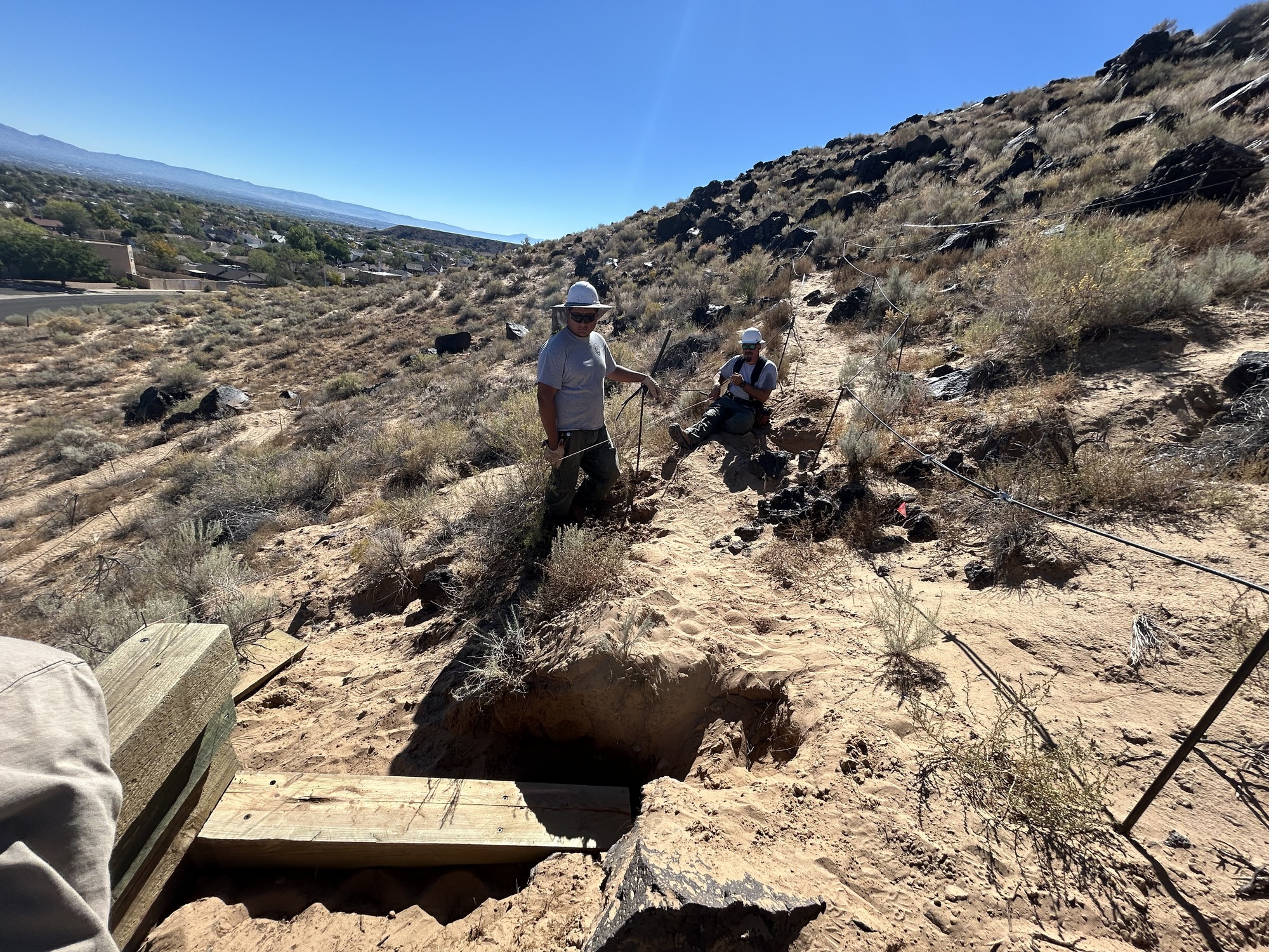 Two workers construct a trail in a desert landscape.