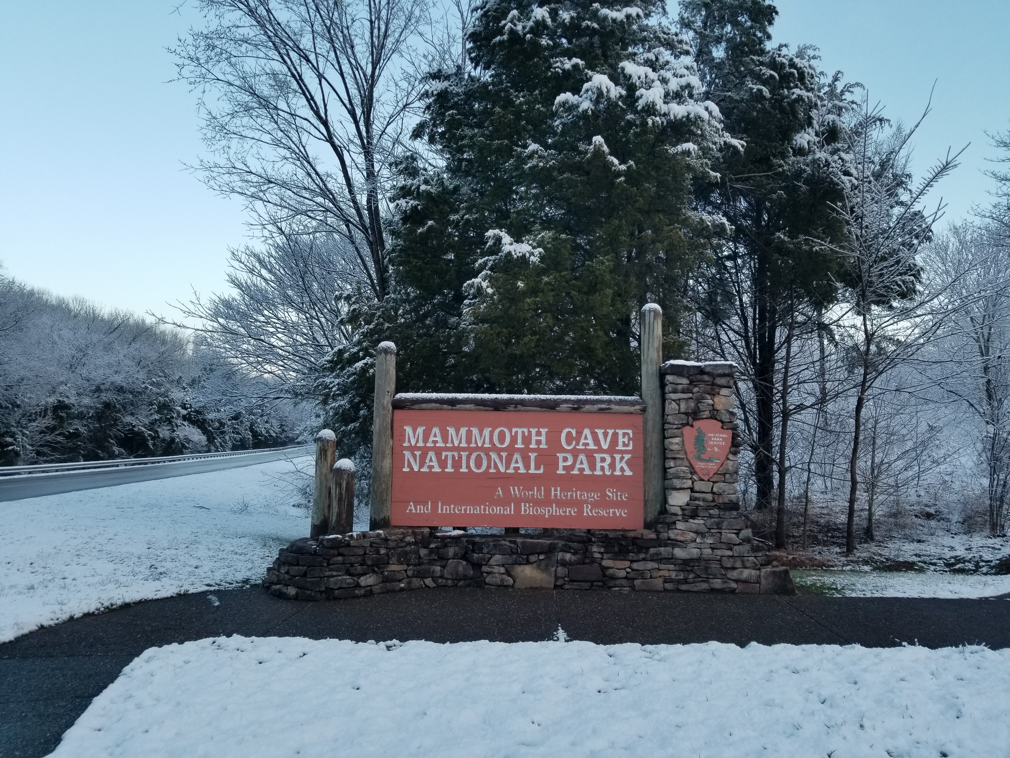 A brown sign stands on a large stone base with snow covering the ground. 