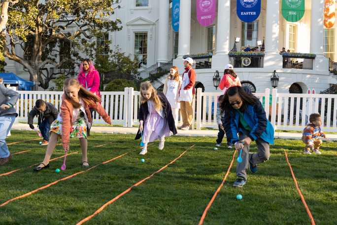 Children play a game of pushing easter eggs down a lane in front of the white house.